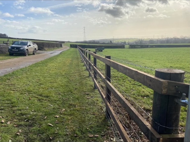 Timber post and rail fencing running alongside a country lane and green field