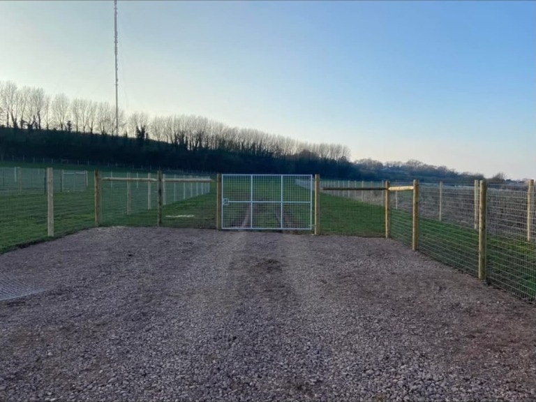 Wire mesh fencing and a metal gate around a gravel entrance to a field