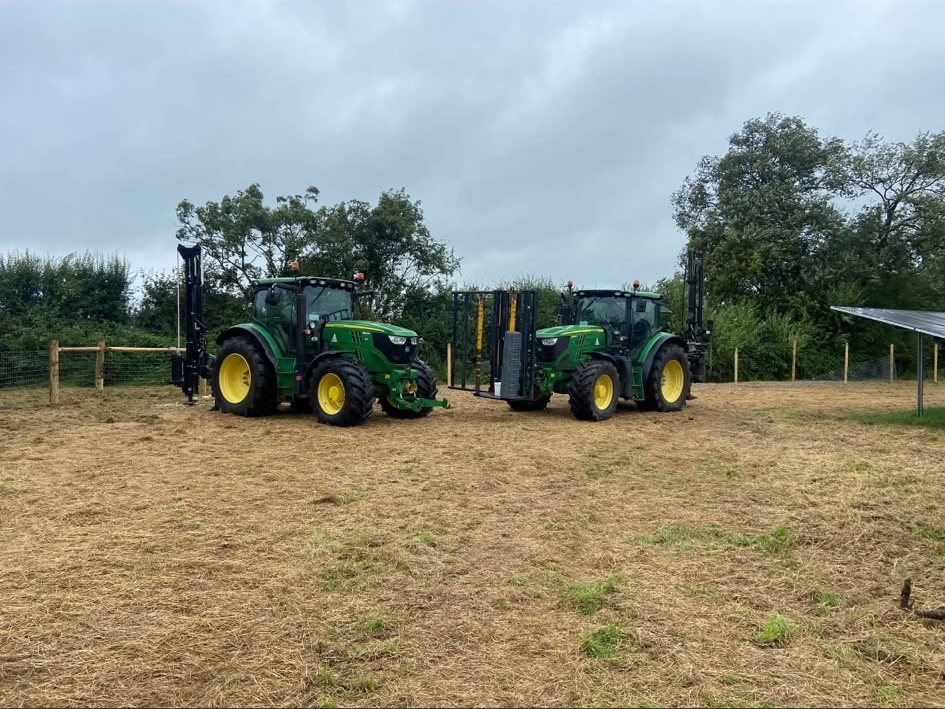 Two green tractors fitted with fencing equipment in a field